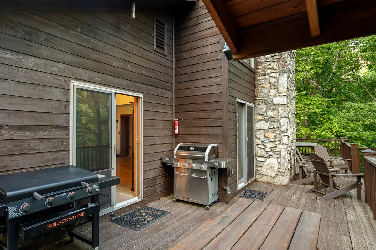 A casual and welcoming deck scene, with a grill, comfortable deck furniture, and a stone feature. The setup invites barbecuing, relaxing, and entertaining, with views that likely extend to the surrounding mountains and forest.