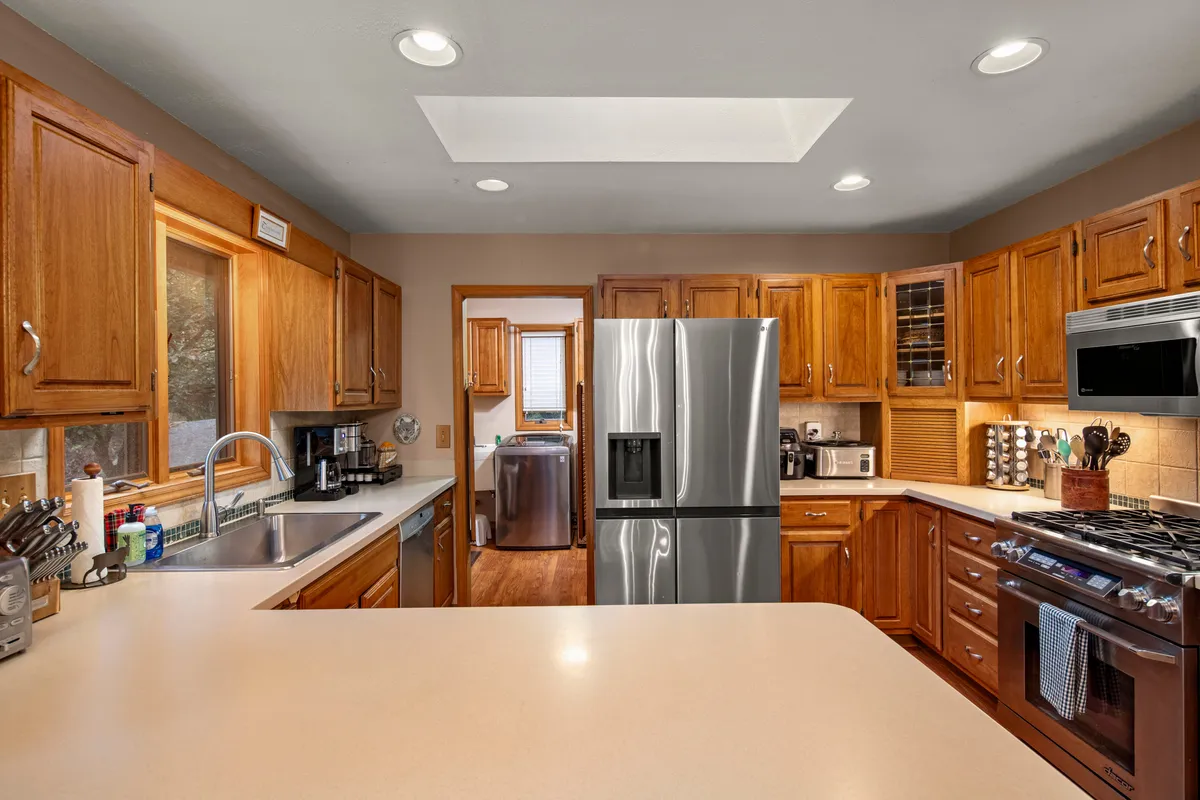 A remodeled kitchen featuring a stainless steel refrigerator, a gas range, a kitchen island, wooden cabinets, and a sink set beneath a window with views outside. The kitchen is spacious, offering plenty of surface area for meal prep and group cooking, and the natural light creates an inviting and homey atmosphere.