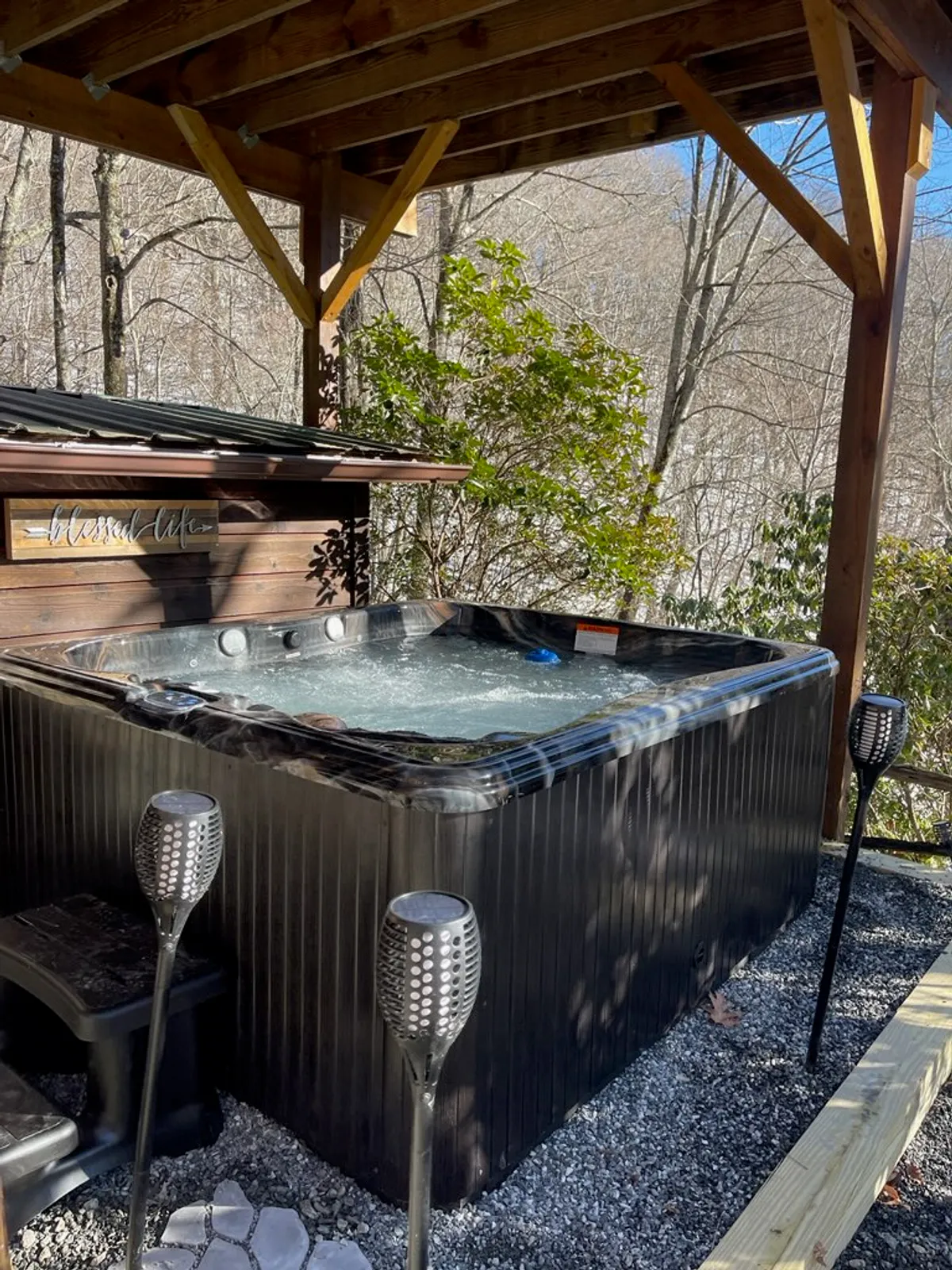 A serene outdoor setting featuring a hot tub surrounded by nature, with decorative torches adding a warm glow. The space invites relaxation, laughter, and unwinding under the stars, epitomizing private comfort after a day of adventure.
