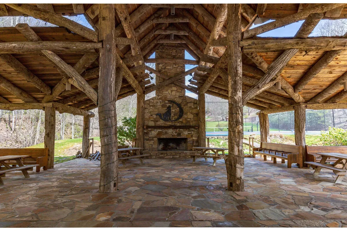 A communal dining area with a stone fireplace, exposed wooden beams, and rustic picnic tables. The space is designed for gathering, sharing meals, and enjoying intimate celebrations in a warm, communal atmosphere.