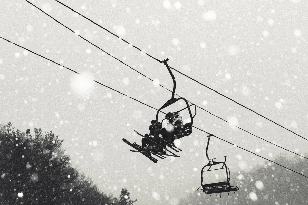 A snow-dusted landscape featuring a ski lift rising through snow-covered trees and gentle snowfall, evoking the magic and adventure of winter activities.
