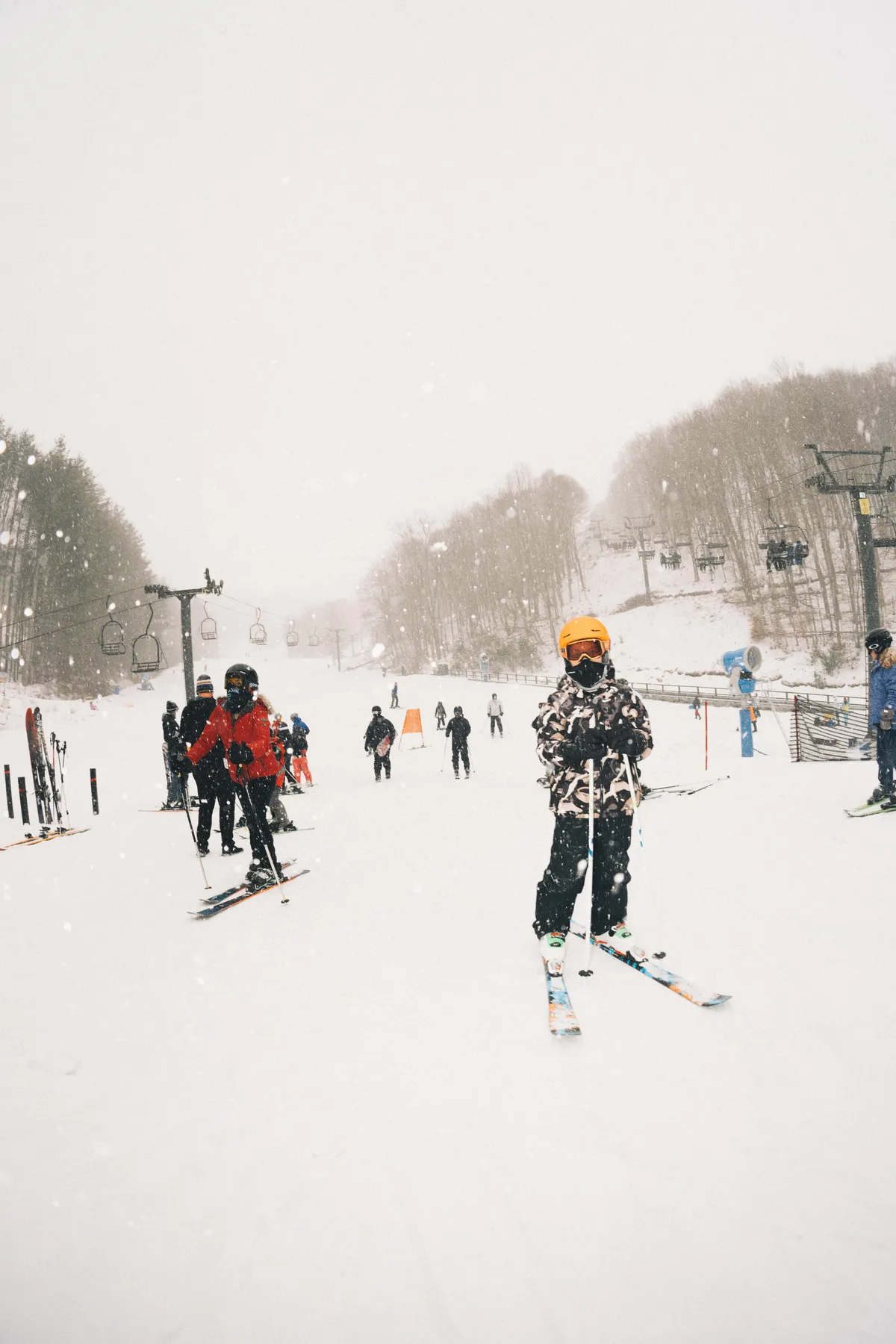 A lively winter scene featuring skiers—adults and a child in bright gear—gliding down a snowy slope, with a ski lift and snow-covered trees in the background. The image captures the energetic, family-friendly atmosphere of winter sports at Hatley Pointe Ski Resort.