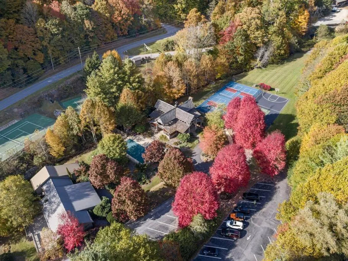 A vibrant exterior shot of the main house flanked by a swimming pool and sports courts, with trees in brilliant autumn hues, highlighting amenities for all ages and skill levels.