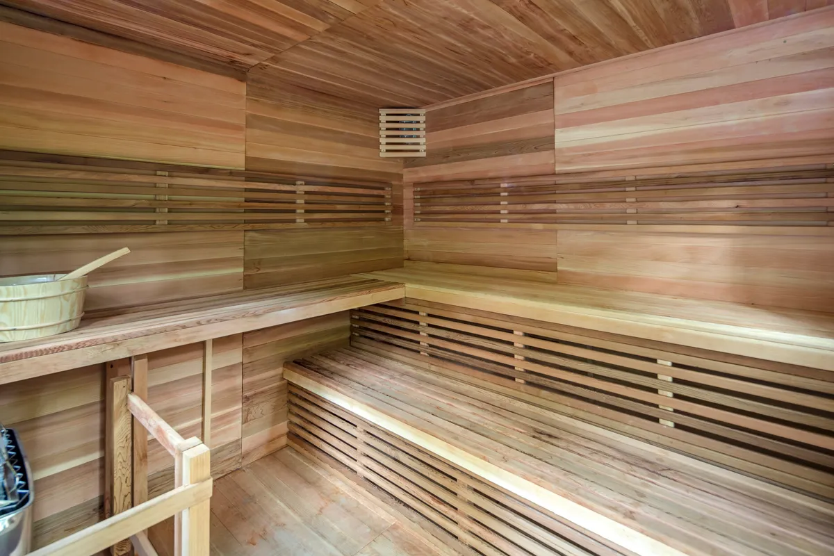 A tranquil sauna interior with wooden benches, a wooden bucket, and soft, ambient ceiling lighting. The enclosed wooden space offers a sense of renewal and calm, ideal for quiet reflection and post-adventure relaxation.